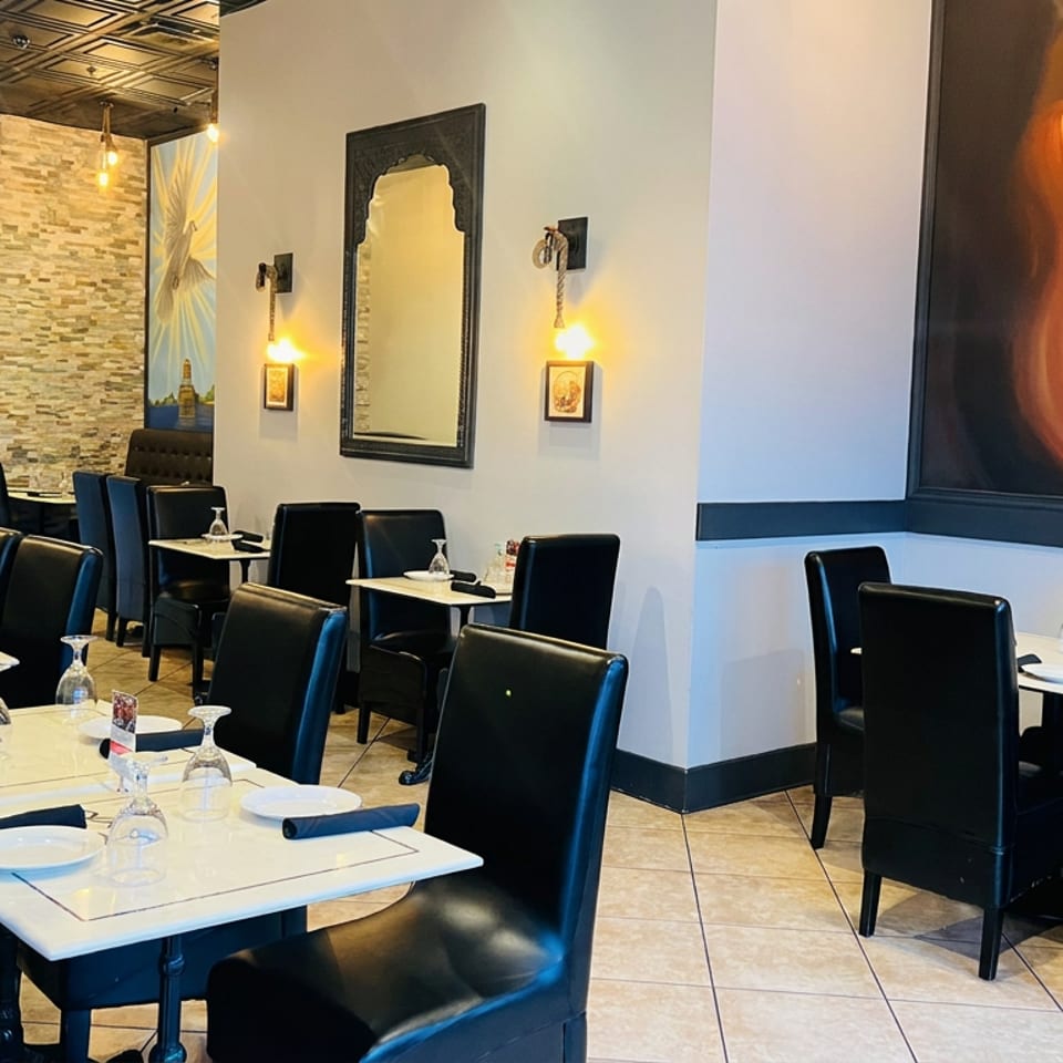 Elegant restaurant dining room with white table settings, black leather chairs, warm lighting, stone walls, and colorful Buddha mural.