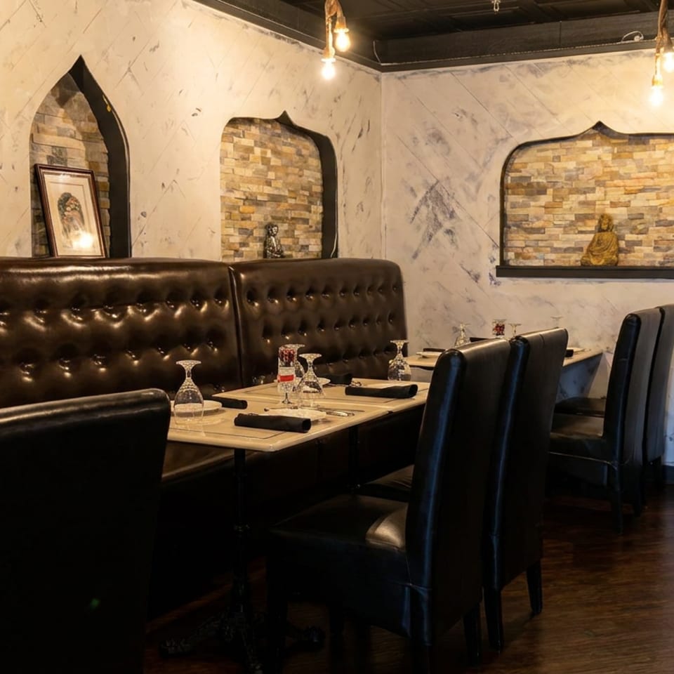 Elegant restaurant dining room with leather booths, set tables, stone wall alcoves, and warm pendant lighting.