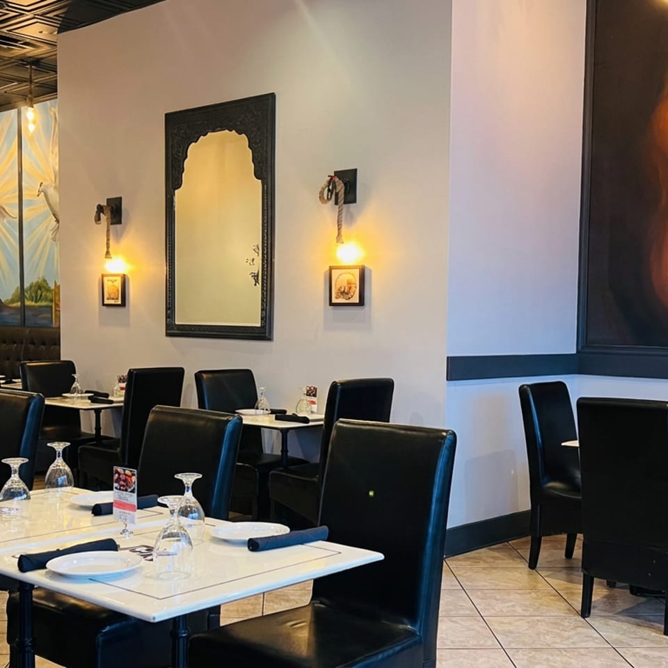 Elegant restaurant dining room with black leather chairs, set tables, warm lighting, stone walls, and a large colorful portrait mural.