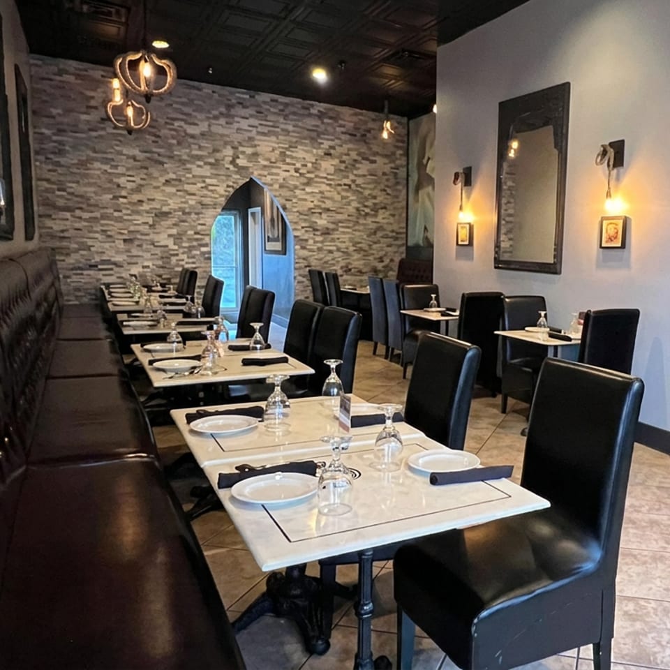 Elegant restaurant dining room with leather banquette seating, neatly set tables, black chairs, stone accent wall, and warm lighting.
