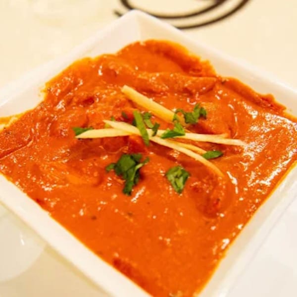 A square white bowl filled with orange Indian curry, garnished with ginger strips and cilantro.
