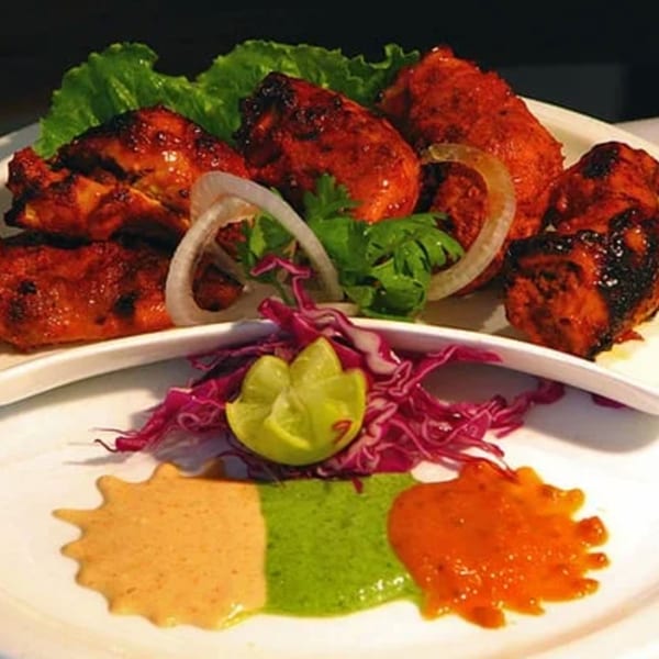 Indian tandoori chicken with lettuce, onions, lime, red cabbage, and three colorful sauces.