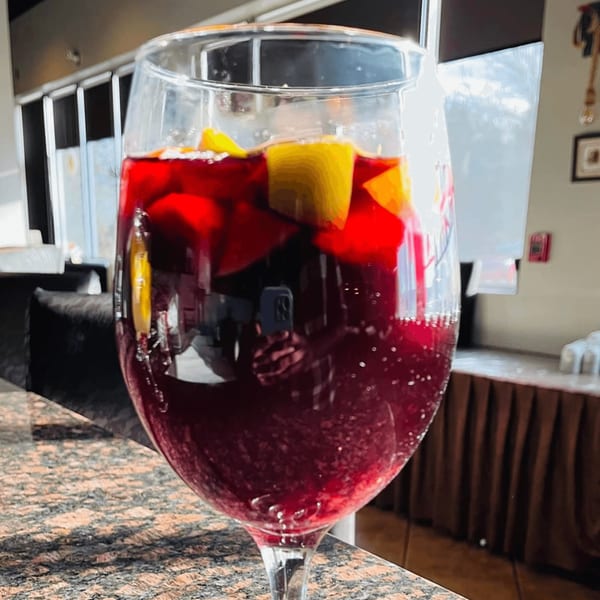 A glass of red sangria with fruit slices sits on a speckled counter at The Mint Indian Cuisine.