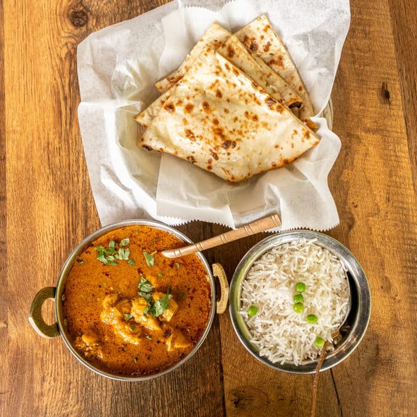 Indian butter chicken, basmati rice with peas, and naan bread on a wooden table.