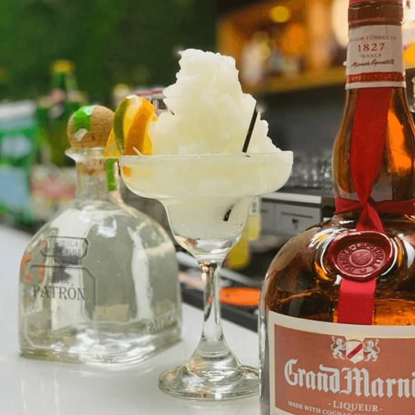 A frozen margarita with lime and orange slices, next to bottles of Patrón and Grand Marnier.