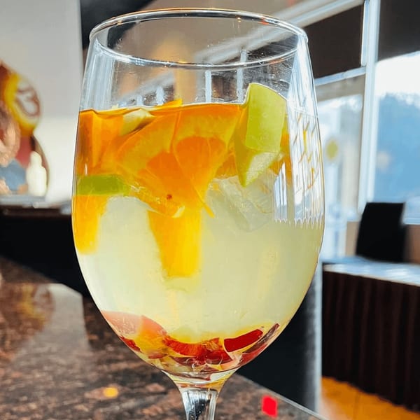 A wine glass filled with a layered drink, featuring orange, yellow, and red fruit pieces.