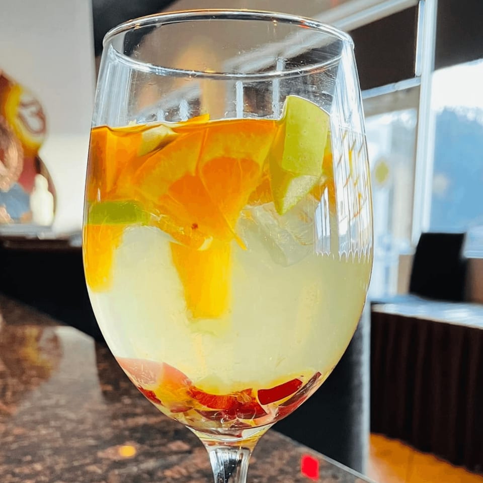A wine glass filled with a layered drink, featuring orange, yellow, and red fruit pieces.