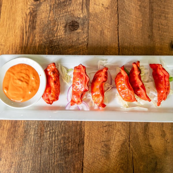 A white rectangular plate of red Indian momos with dipping sauce, on a wooden table.