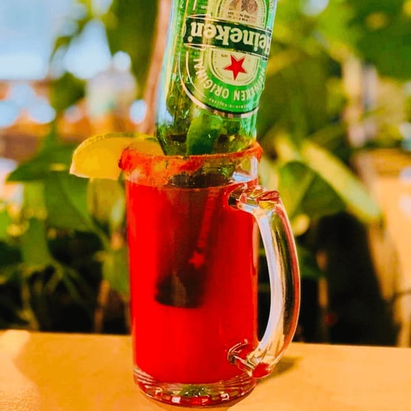 A red drink in a mug with a Heineken bottle inverted into it, garnished with lime.
