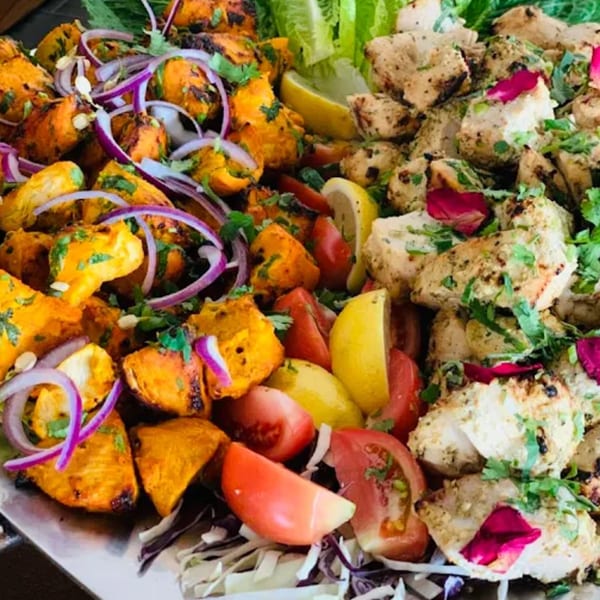 Platter of Indian chicken tikka and malai tikka, garnished with onions, tomatoes, and lemon.