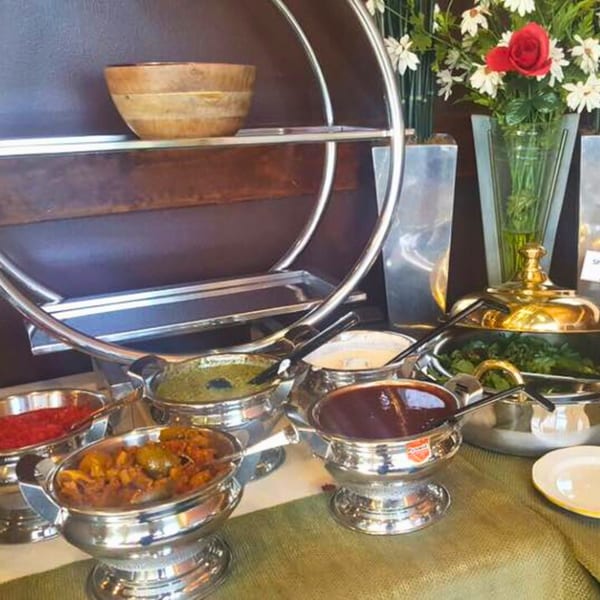 Indian buffet with various curries, chutneys, and salads in silver serving dishes.
